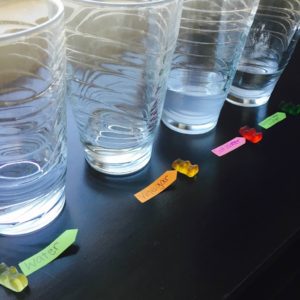 4 clear cups with different solutions and gummy bears outside of the cups