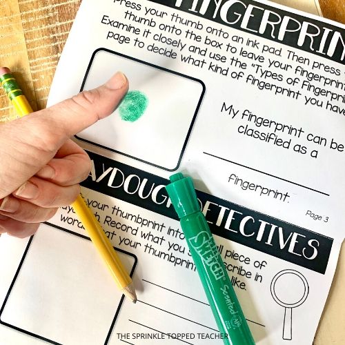 Student thumb making green fingerprint in the science project workbook.