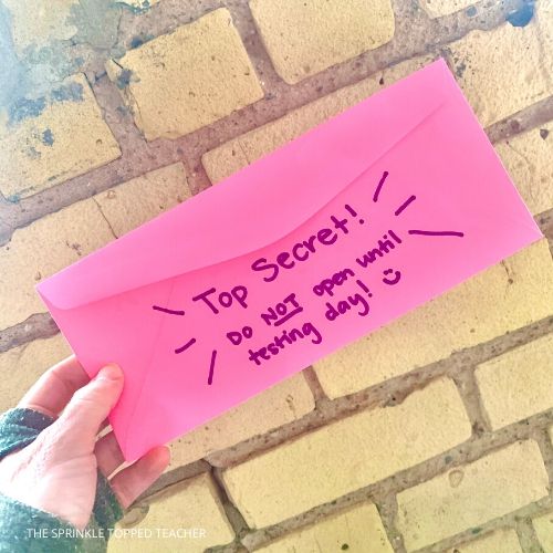 Pink envelope with text: top secret, do not open until testing day. Set in front of brick background.