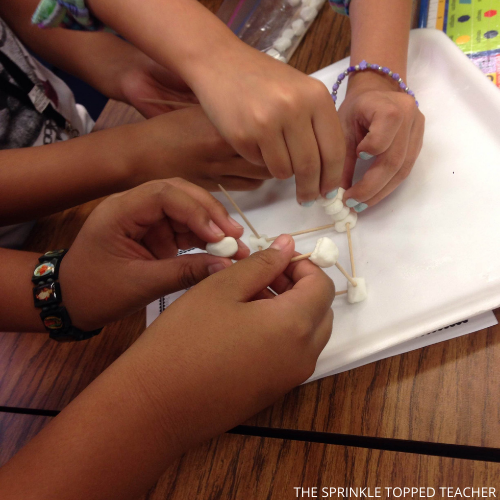 student hands working to build a toothpick tower with marshmallows