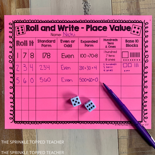 Purple pen on pink paper with a set of dice for the place value game in 2nd grade