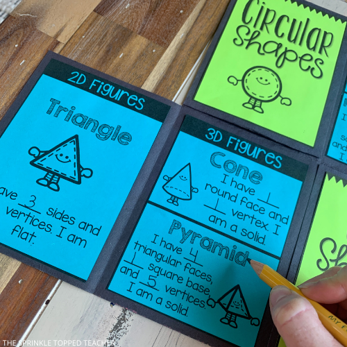 Blue and green foldable being opened by a hand. The second grade geometry foldable is sectioned into four parts: circular shapes, quadrilateral shapes, triangular shapes, and other shapes. This image features the triangle, cone and pyramid.
