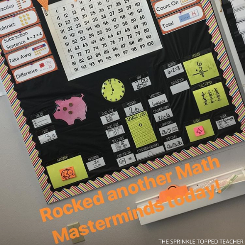 Math Masterminds bulletin board displaying the 2nd Grade Math Warm Up and all its elements. Includes time, piggy bank, money, measurement, numbers charts, comparing and more. The caption says, "Rocked another math masterminds today!"