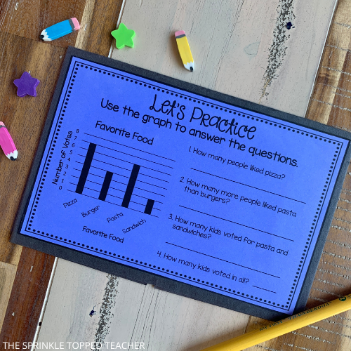 This blue half sheet of the graphing foldable says "let's practice". Students use the graph to answer 4 fill in the blank questions. There are colorful mini erasers and a student pencil next to the page.
