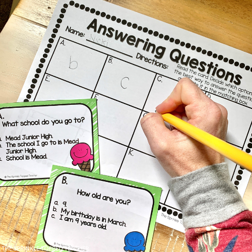 Student writing with a pencil on the answer sheet. Question tasks cards with multiple choice answers.